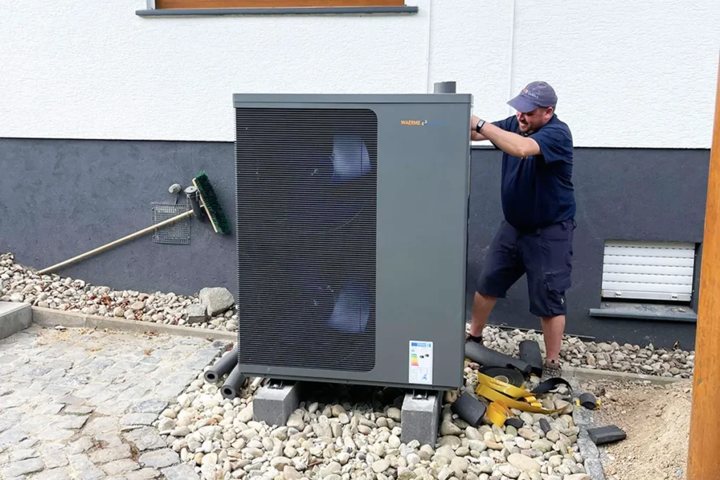 Ein Techniker der Waermequelle GmbH beim Einbau einer Wärmepumpe vor einem Haus.