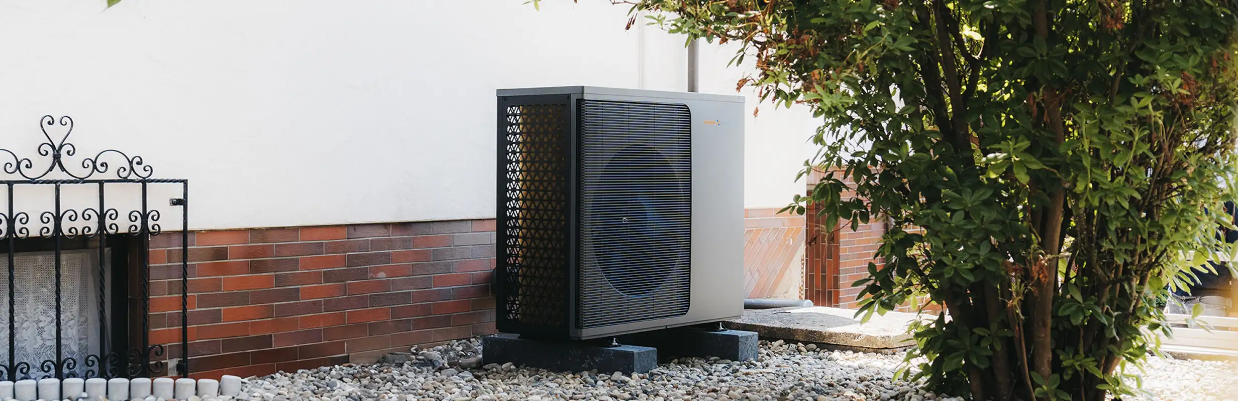 Eine Wärmepumpe der Waermequelle GmbH auf Kieselsteinen vor einer weißen Hauswand.