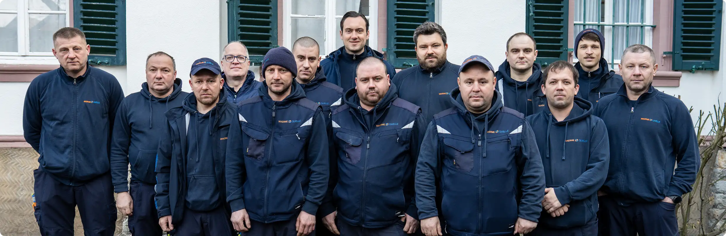 Gruppenbild des Teams der Waermequelle GmbH in dunkelblauer Arbeitskleidung vor einer Hauswand.